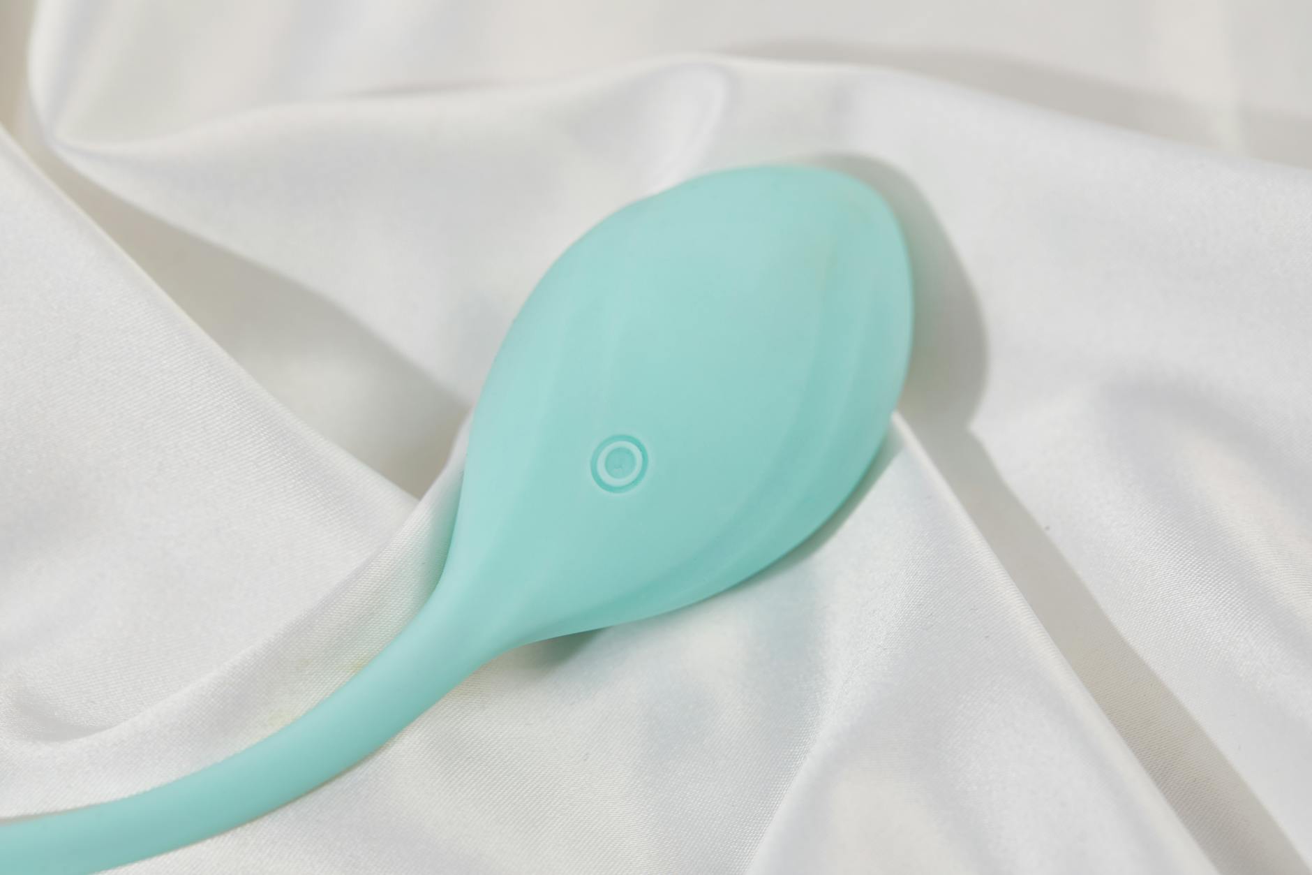 A stylish teal vibrator on smooth white silk fabric, representing clitoral vibrator design