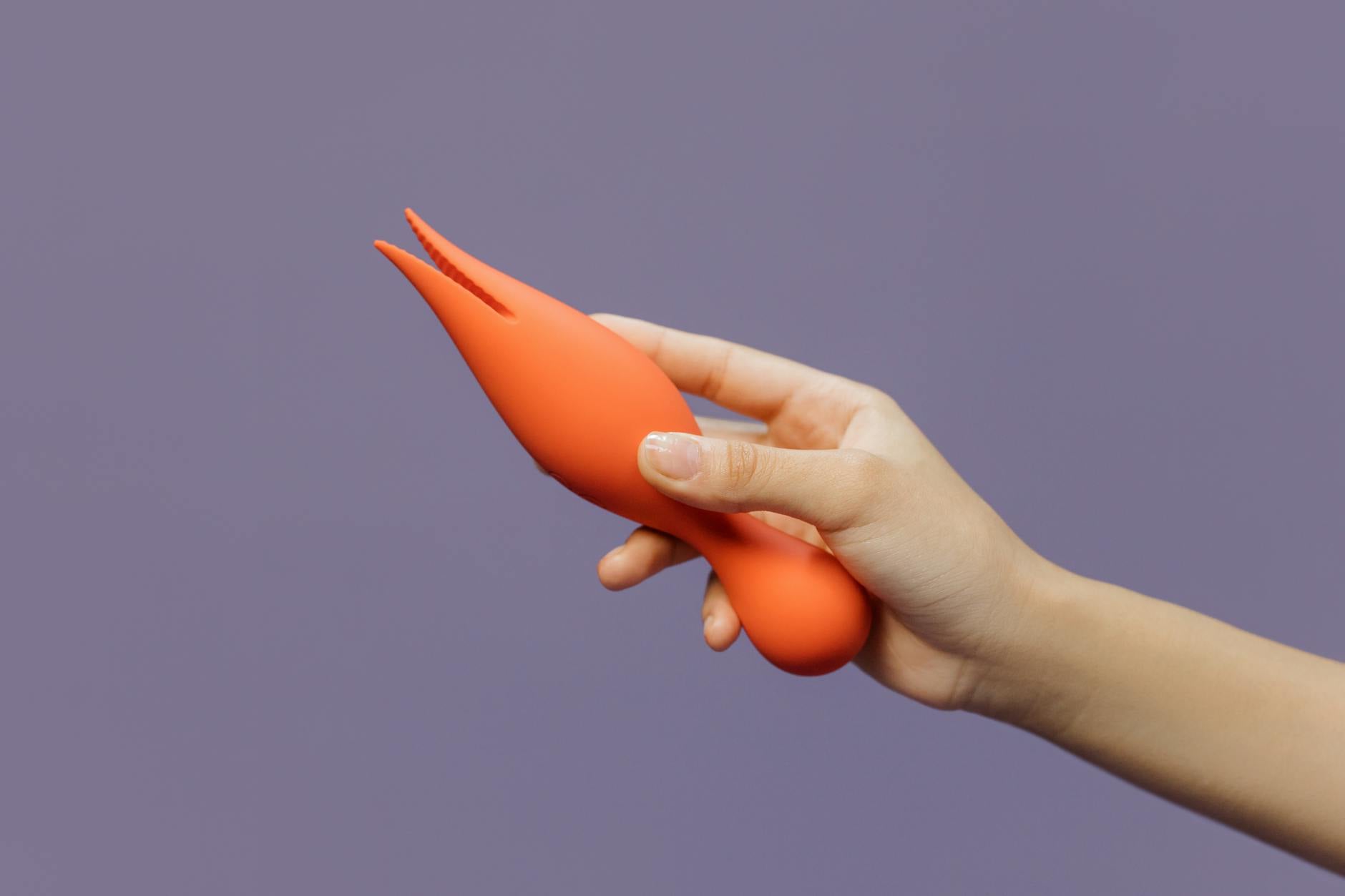 Close-up of a hand holding a lemon-colored vibrator against a minimalist backdrop