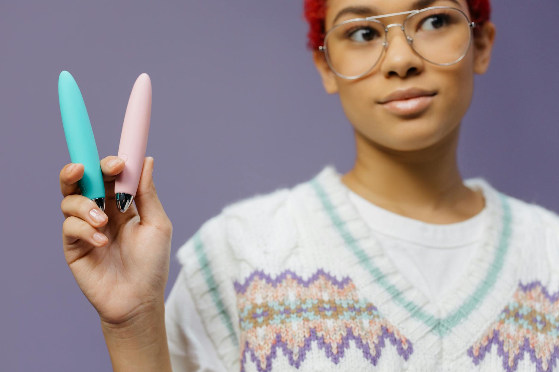 A woman holds two vibrators against a purple background, ready to explore pleasure with intentional tools