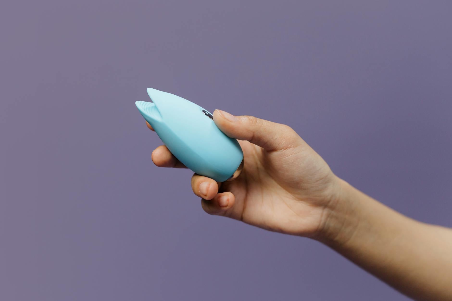 A blue silicone vibrator held in hand against a solid purple background, symbolizing sensual touch and pleasure recovery