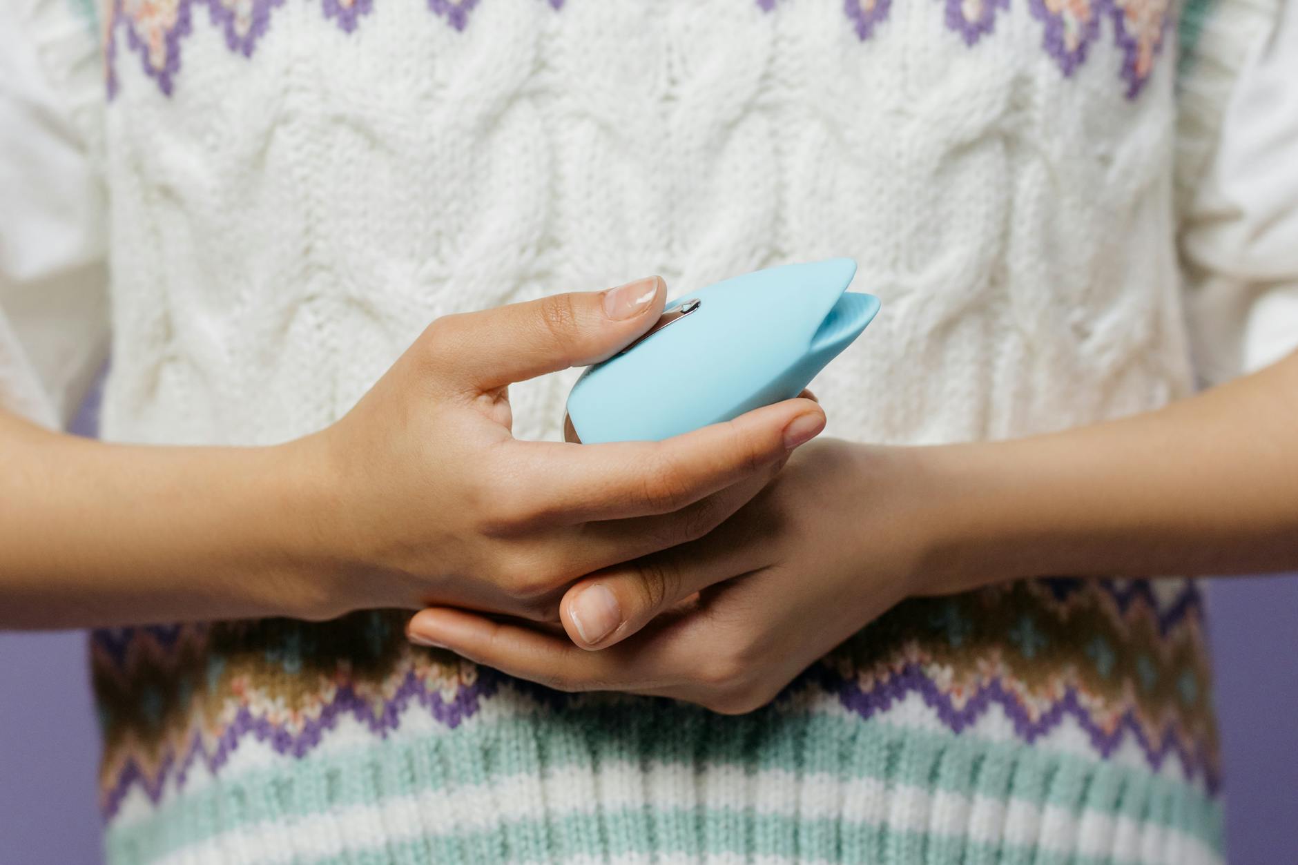 Close-up of hands holding a lemon clitoral vibrator against a knitted sweater.