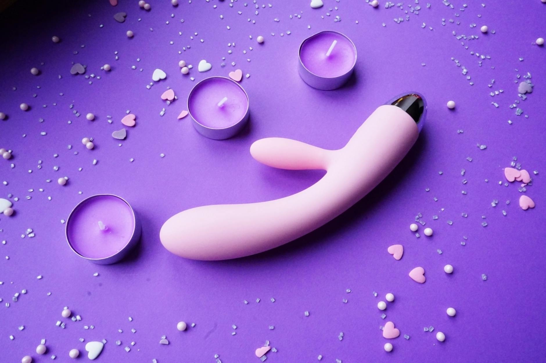 Lemon clitoral vibrator on pink background with romantic candles and heart confetti